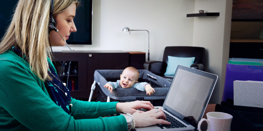 A mother works on a computer while her baby reaches out for her attention