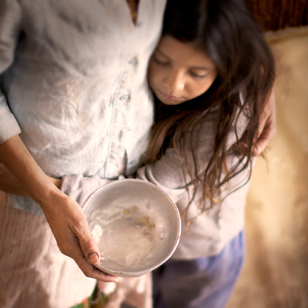 A woman holds an empty bowl and embraces a little girl