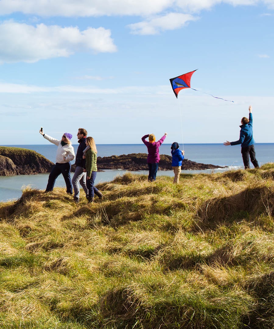 People at the seashore fly a kite and take pictures