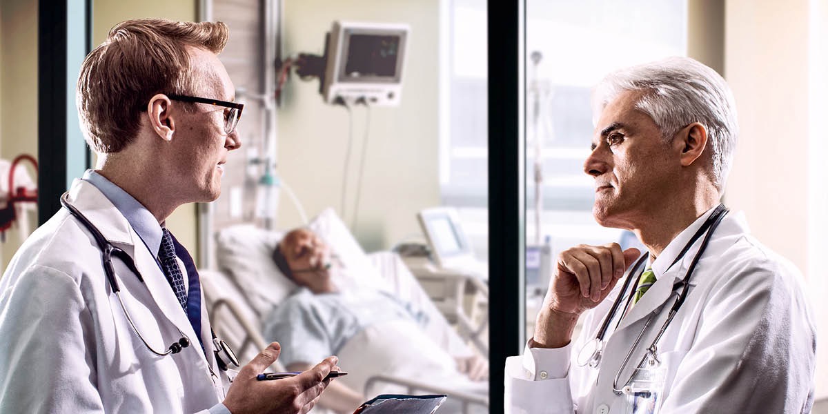 Two doctors confer outside a man’s hospital room