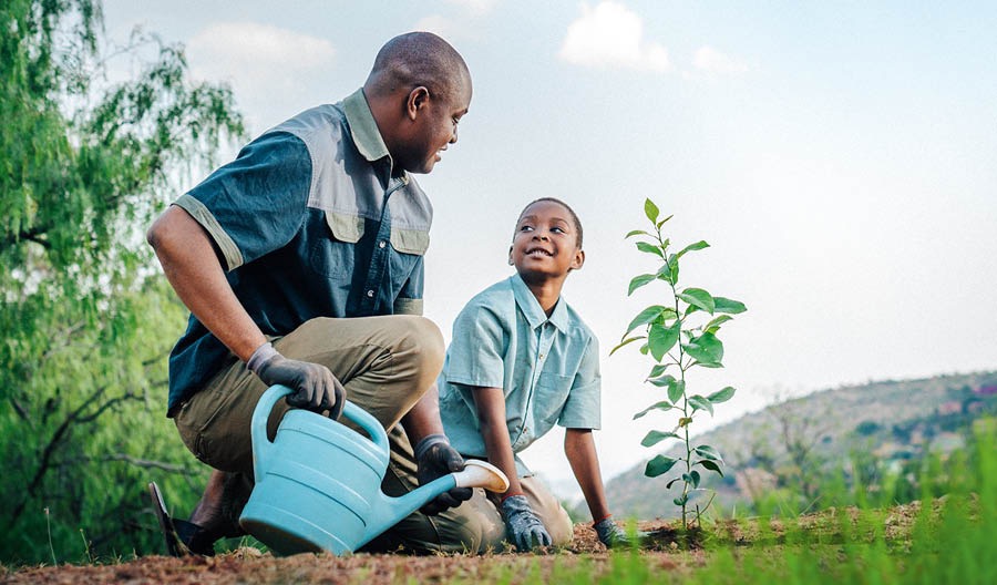 A father helps his son to water a plant