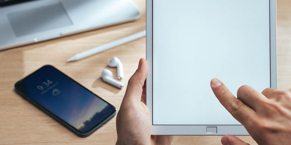 Someone using a tablet. Other electronic devices sit on a nearby table.