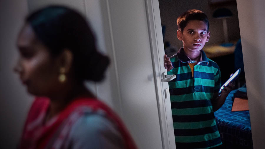 A boy holding a smartphone and nervously closing his bedroom door as his mother walks by.