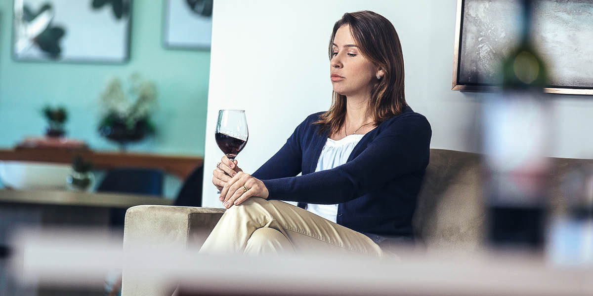 A woman staring at her glass of wine while sitting alone at home.