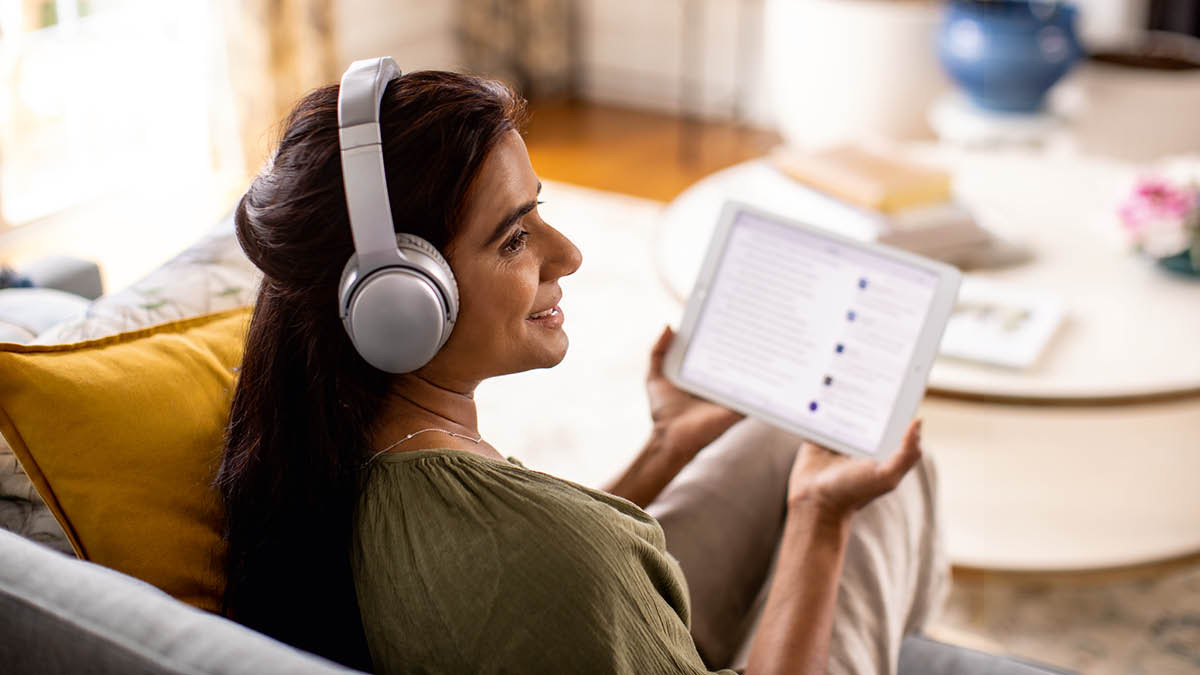 A sister wearing headphones and listening to an audio recording on her tablet.