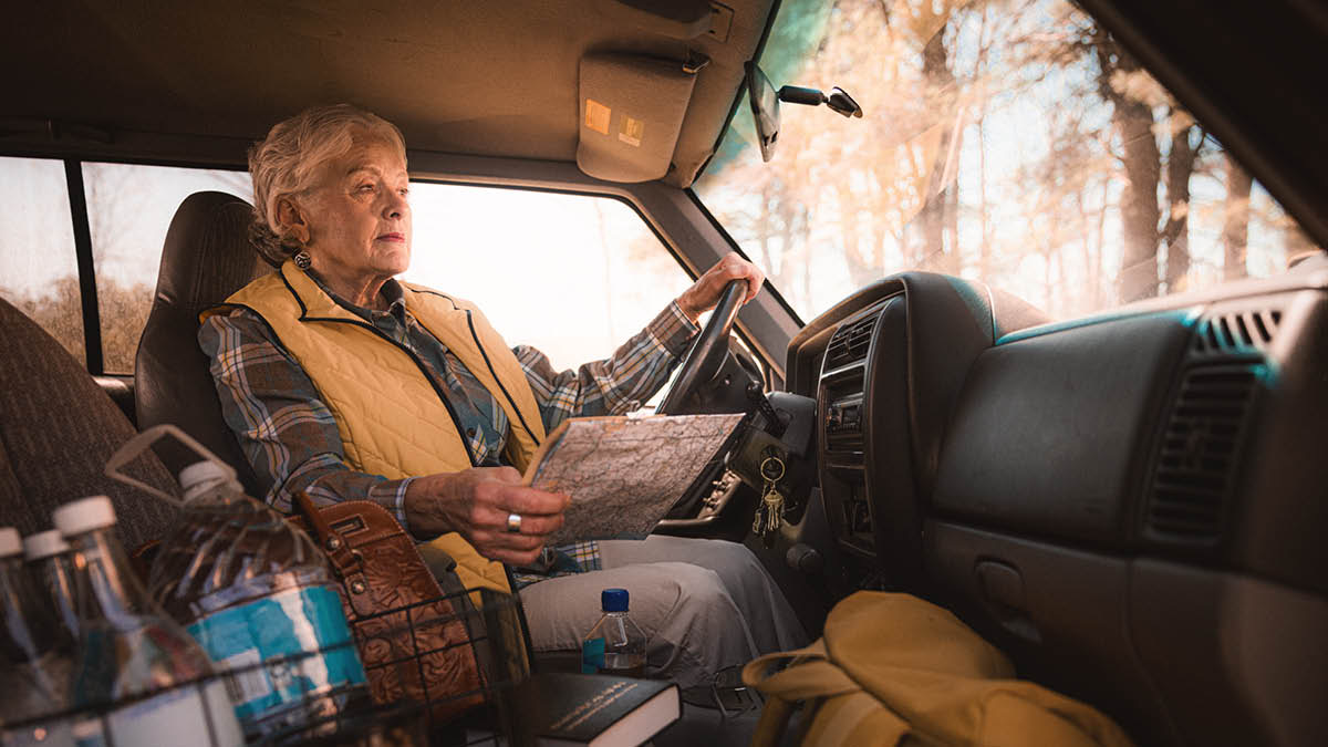 A sister holding a map as she sits in her car. She has bottles of water and other supplies with her.