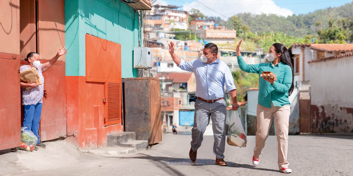 A couple wearing facemasks, delivering food items to an elderly sister.