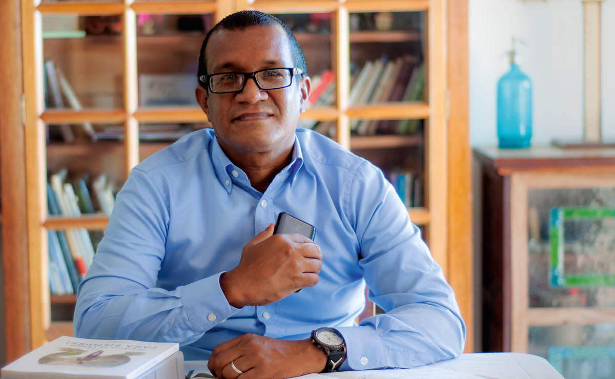 Argenis sitting at his desk with a phone, a Bible, and the book “Enjoy Life Forever!”