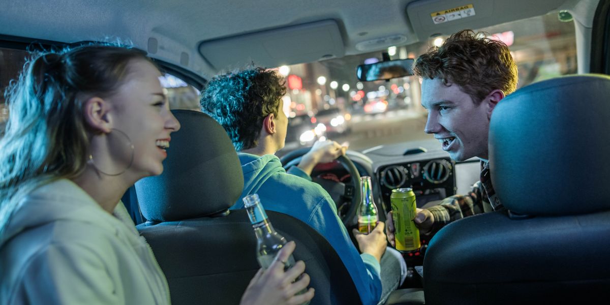 A young adult driving a car while he and his friends drink alcoholic beverages.