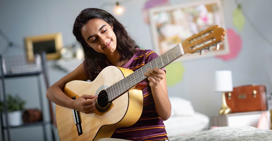 A teenage girl in her bedroom playing a guitar.
