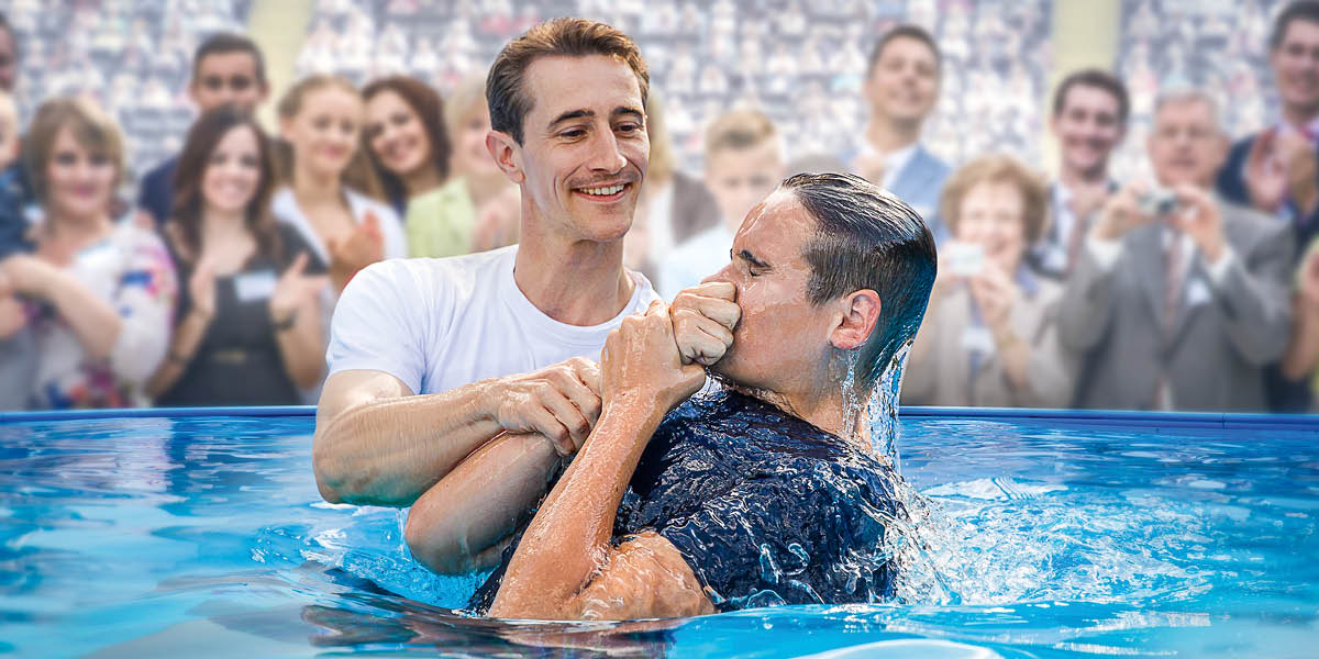 A young man getting baptized in a pool at a convention of Jehovah’s Witnesses.