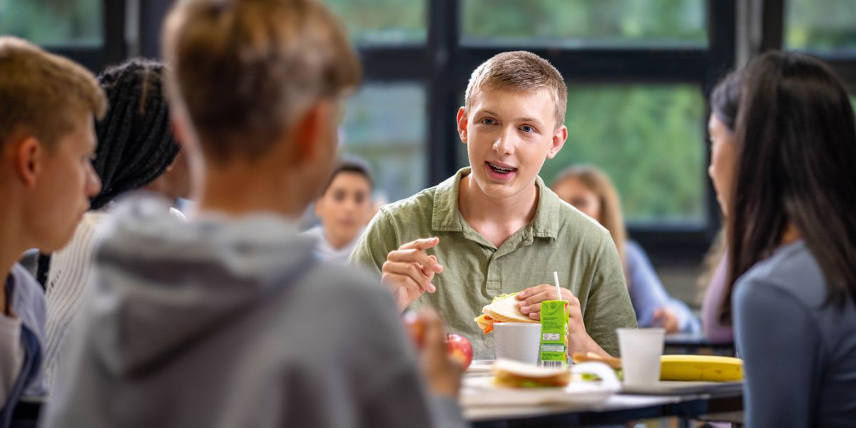 A teenage boy conversing with a few of his schoolmates during lunch.