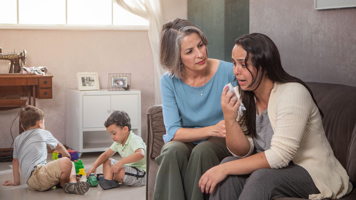 A sister listening empathetically to a single mother in distress. The mother’s two young sons play in another room.