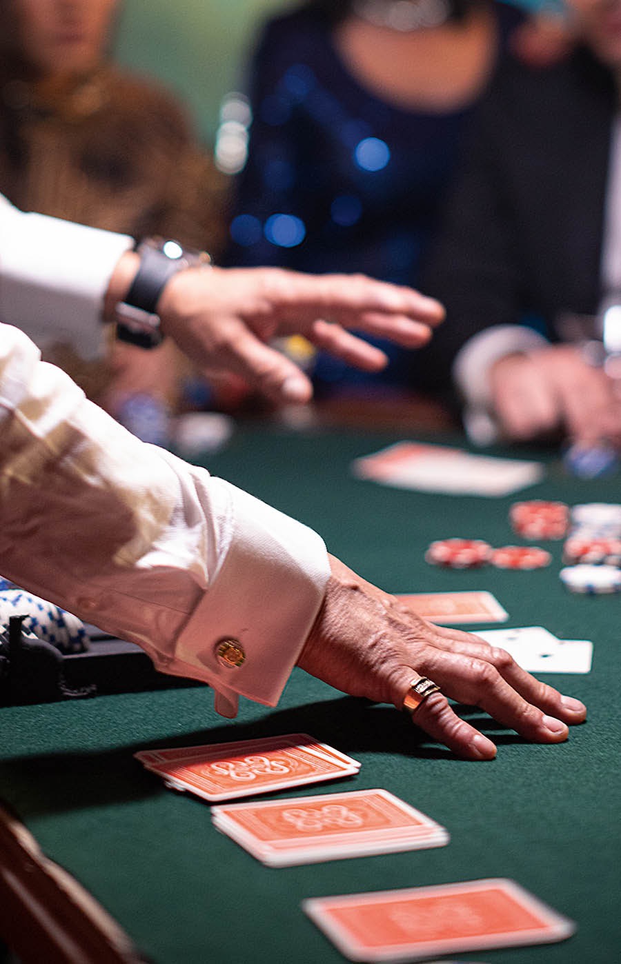 A man dealing cards at a casino gaming table as gamblers look on.