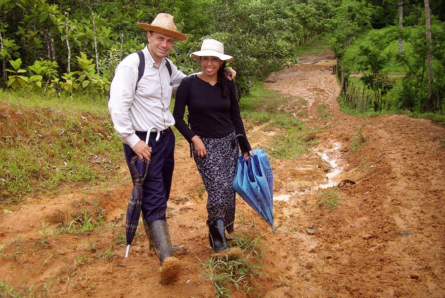 Donald and his wife, Nuria, standing in a muddy road. They are outfitted with hats, backpacks, umbrellas, and rubber boots.