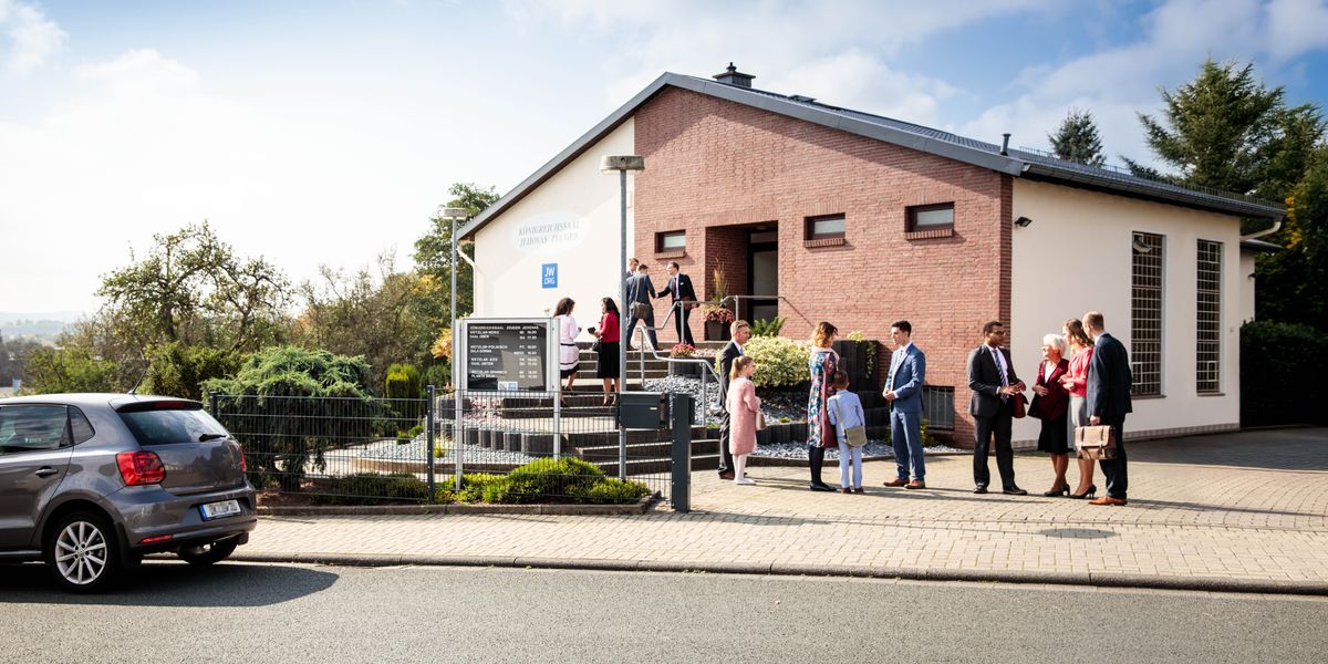 A group of Jehovah’s Witnesses warmly speaking with one another outside a Kingdom Hall.