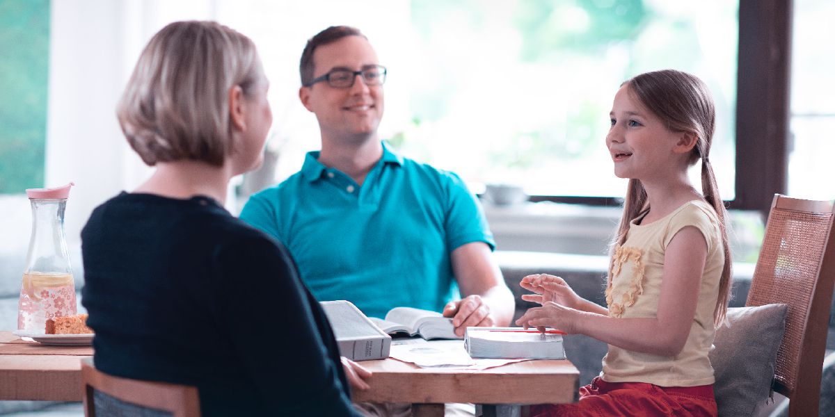 A daughter smiling as her father and mother teach her about the Bible.
