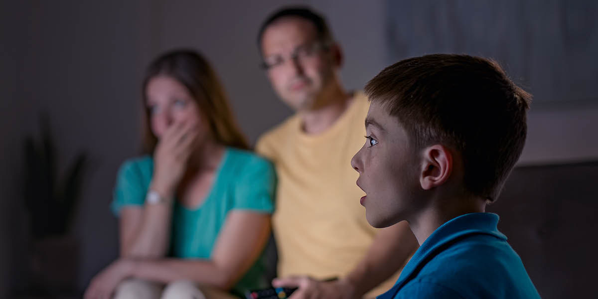 A family watching TV. The father realizes that a disturbing news report is affecting his son.