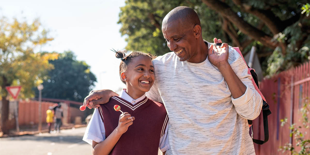 A father and his teenage daughter happily walking down a street.
