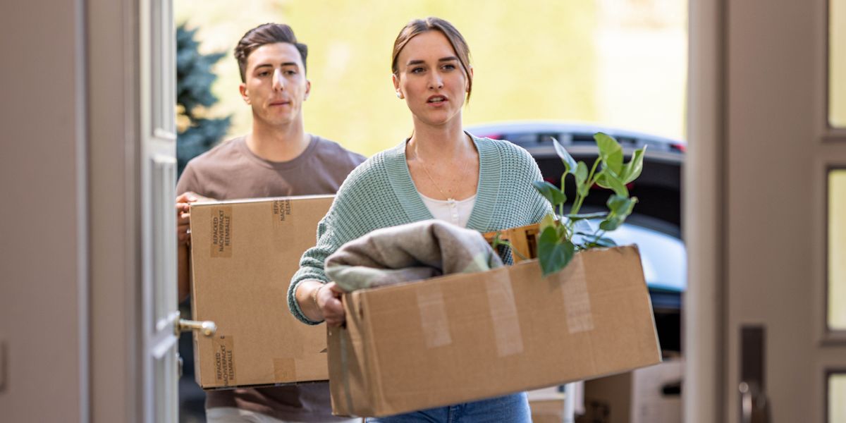 A man and a woman carrying boxes of personal items into their house.