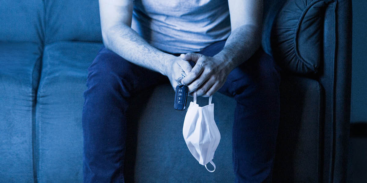 A man sitting on a couch, holding car keys and a face covering.