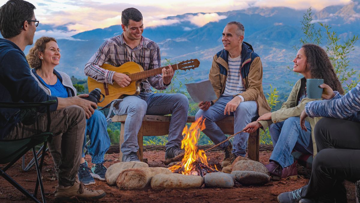 Friends sitting around a campfire. One of them is playing the guitar.