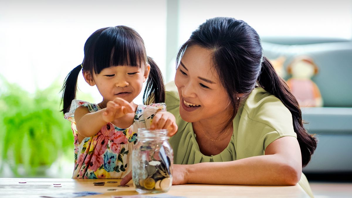 A young girl dropping coins into a jar as her mother joyfully observes.