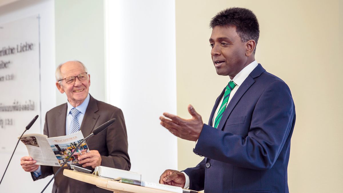 A younger elder conducting the “Watchtower” Study while an older brother, who is the reader, smiles at him.